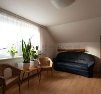 Wohnzimmer mit Holzboden-Dekor, dunklem Sofa und Korbsesseln in einem Einfamilienhaus.