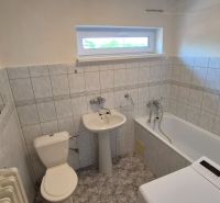 Badezimmer in einer 2-Zimmer-Wohnung mit Badewanne, Waschbecken, Waschmaschine und gefliesten Wänden.