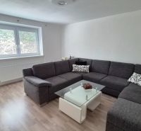 Wohnzimmer mit einer grauen Eckcouch und einem Tisch, Holzboden mit Holzdekor.