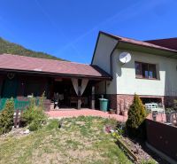 Ein Einfamilienhaus in Švošov mit Terrasse und Garten, umgeben von Bergen und blauem Himmel.