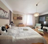 Schlafzimmer in einem Einfamilienhaus mit Bett, Bildern und Sessel, Boden mit Holzdekor.