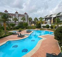Ferienwohnungen in Kumköy, SIDE, mit einem Pool, umgeben von Liegestühlen und Palmen.