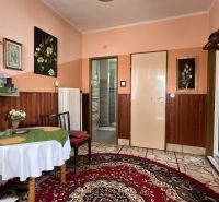 Ein Zimmer in einem Einfamilienhaus, dekoriert mit Bildern, einem Tisch mit Tischdecke und einem Teppich.