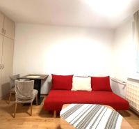 Ein Zimmer in einer Ferienwohnung mit einem roten Sofa, einem Tisch und einem Boden in Holzoptik.