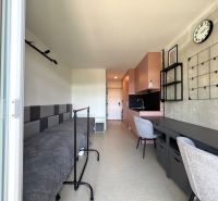 Innenraum eines Studios mit Bett, Tisch und Küchenzeile in sanften Farben.