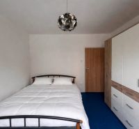 Schlafzimmer in einer 2-Zimmer-Wohnung mit Bett, Kleiderschrank und blauem Boden.