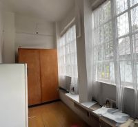 Ein Flur mit großen Fenstern, Holzboden, einem Schrank und einem weißen Kühlschrank.