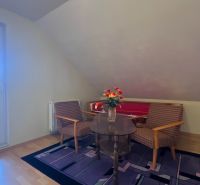 Ein Zimmer mit Sesseln und einem Tisch, ein Boden mit Holzdekor, Blumen auf dem Tisch.