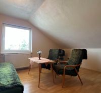 Ein Zimmer in einem Einfamilienhaus mit einem Boden in Holzoptik, einem Sofa und Sesseln.