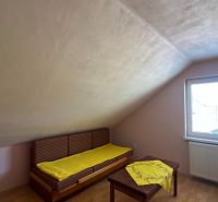 Ein Dachzimmer in einem Einfamilienhaus mit Fenster und Bett, Boden mit Holzdekor.