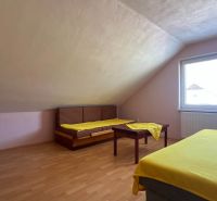 Ein helles Dachzimmer mit zwei Betten, einem Tisch und einem Boden in Holzoptik.