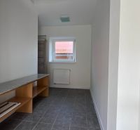 Ein schmaler Raum mit einem Fenster, einem Heizkörper, Regalen und einem grauen Boden in einem Einfamilienhaus.