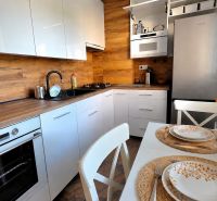 Küche in einer 2-Zimmer-Wohnung mit weißen Schränken, Holzboden und einem Tisch mit Blumen.