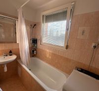 Badezimmer in einer 3-Zimmer-Wohnung mit Badewanne, Waschbecken und Waschmaschine, Fliesen in warmen Tönen.