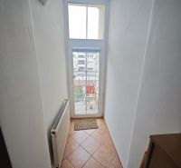 Ein schmaler Flur mit einem Fenster und einem Heizkörper in einer 2-Zimmer-Wohnung, Fliesen auf dem Boden.