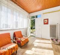 Innenraum eines Einfamilienhauses mit Sesseln, großen Fenstern und einem Boden in Holzoptik.