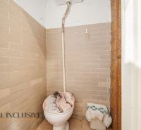 Einfaches Badezimmer mit Toilette, gefliest mit beigefarbenen Fliesen in einem Einfamilienhaus.