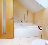 Badezimmer in der Hütte mit Badewanne und hellen Fliesen, Boden mit Holzdekor.