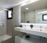 Badezimmer in einer 2-Zimmer-Wohnung mit Doppelwaschbecken, Spiegel und Duschkabine.