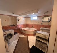 Badezimmer in einem Einfamilienhaus mit Badewanne, Waschmaschine, Waschbecken und Boden mit Holzdekor.