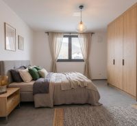 Helles Schlafzimmer mit Holzmöbeln, grauen Accessoires und großem Fenster.