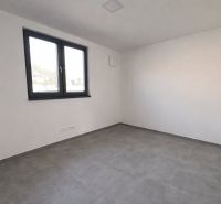 Ein leerer Raum mit Fliesenboden, weißen Wänden und einem großen Fenster in einem Einfamilienhaus.