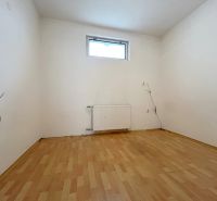Ein Zimmer in einem Einfamilienhaus mit einem Boden in Holzoptik und einem Heizkörper unter dem Fenster.