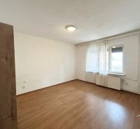 Ein Zimmer in einem Einfamilienhaus mit einem Boden in Holzoptik und Fenstern mit weißen Vorhängen.