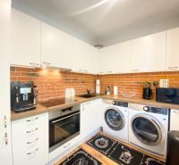 Küche in einer 2-Zimmer-Wohnung mit weißen Möbeln, Ziegelverkleidung und Geräten.