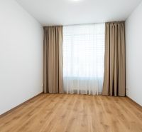 Ein Zimmer in einer 3-Zimmer-Wohnung mit einem Boden in Holzoptik und Vorhängen am Fenster.