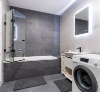 Badezimmer in einer 3-Zimmer-Wohnung mit Badewanne, Waschmaschine und beleuchtetem Spiegel.