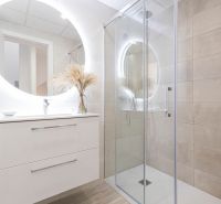 Badezimmer in der Ferienwohnung mit großem beleuchtetem Spiegel und Duschkabine.