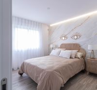 Schlafzimmer in einer Ferienwohnung mit Bett, Stoffvorhängen und einem Boden in Holzoptik.