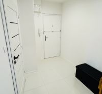Weißer Eingangsflur mit Fliesen und dunkler Bank in einer Einzimmerwohnung.