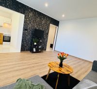 Wohnzimmer einer Einzimmerwohnung mit Holzboden und Blumen auf dem Tisch.