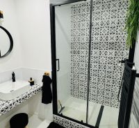 Badezimmer mit Duschkabine und gemusterten Fliesen in einer Einzimmerwohnung.