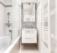 Badezimmer in einer 2-Zimmer-Wohnung mit Badewanne, Spiegel und Fliesen mit Mosaikdekor.