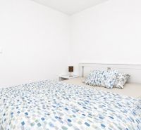 Schlafzimmer in einer 2-Zimmer-Wohnung mit Bett und Holzboden, weiße Wand, Nachttische.