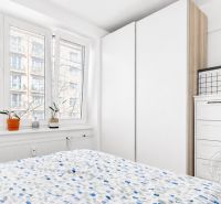 Helles Schlafzimmer mit großem Fenster, weißem Kleiderschrank und Kommode in einer Zweizimmerwohnung.