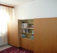 Ein Zimmer in einer 2-Zimmer-Wohnung mit einem Bücherregal und einem großen Schrank, Boden mit Holzdekor.