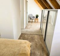 Dachzimmer mit Holzboden in einer 3-Zimmer-Wohnung, helle Wände und ein bequemer Sessel.
