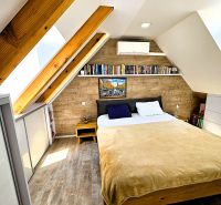 Ein Schlafzimmer im Dachgeschoss mit Holzbalken, einem Bücherregal und einem Boden mit Holzdekor.