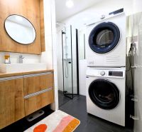 Badezimmer in einer 3-Zimmer-Wohnung mit Waschmaschine, Trockner, Duschkabine und Boden mit Holzdekor.