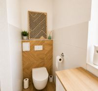 Helles Badezimmer mit Holzelementen und interessanter Wanddekoration in einer Zweizimmerwohnung.