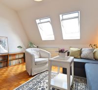 Wohnzimmer in einer 2-Zimmer-Wohnung mit Holzboden, bequemer Couch und Sessel.