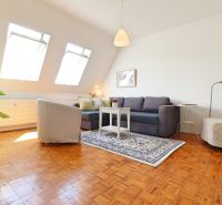 Wohnzimmer in einer 2-Zimmer-Wohnung mit Holzboden und hellen Dachfenstern.