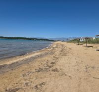 Sandstrand mit Strohdächern in Privlaka, mit blauem Himmel und Meer.