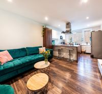 Wohnzimmer mit Küchenzeile in einer 3-Zimmer-Wohnung, Boden mit Holzdekor, grünes Sofa.
