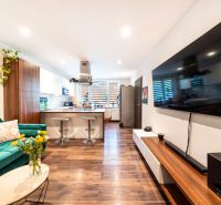 Wohnzimmer in einer 3-Zimmer-Wohnung mit Fernseher, Sofa und Küche, Boden mit Holzdekor.