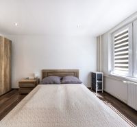 Schlafzimmer mit Bett, Holzboden und großen Fenstern in einer 3-Zimmer-Wohnung.